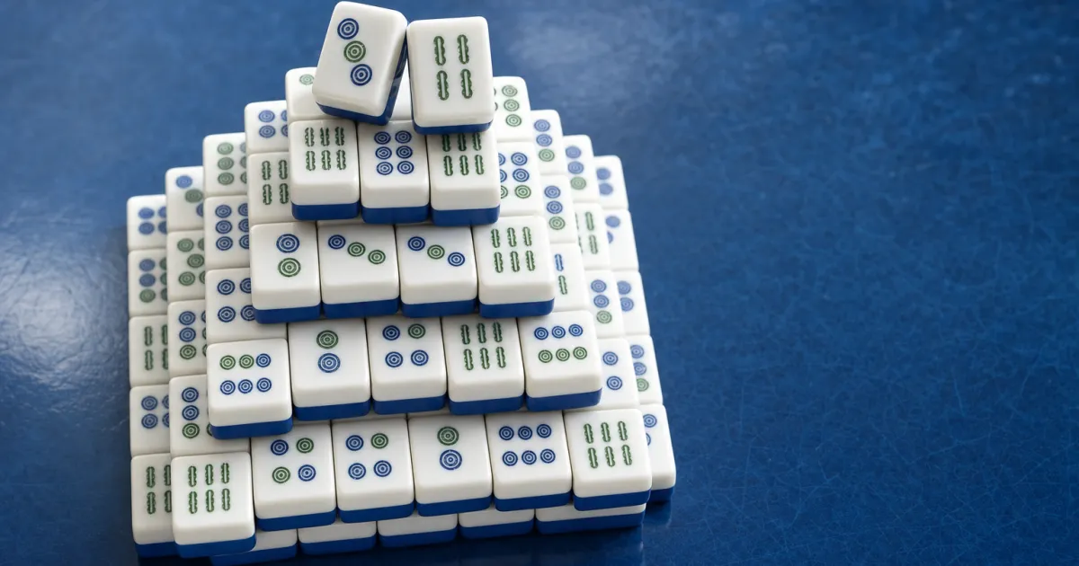 En stak hvide mahjong-brikker med koboltblå bagside formet som en pyramide på et blåt bord, med to brikker løftet af toppen